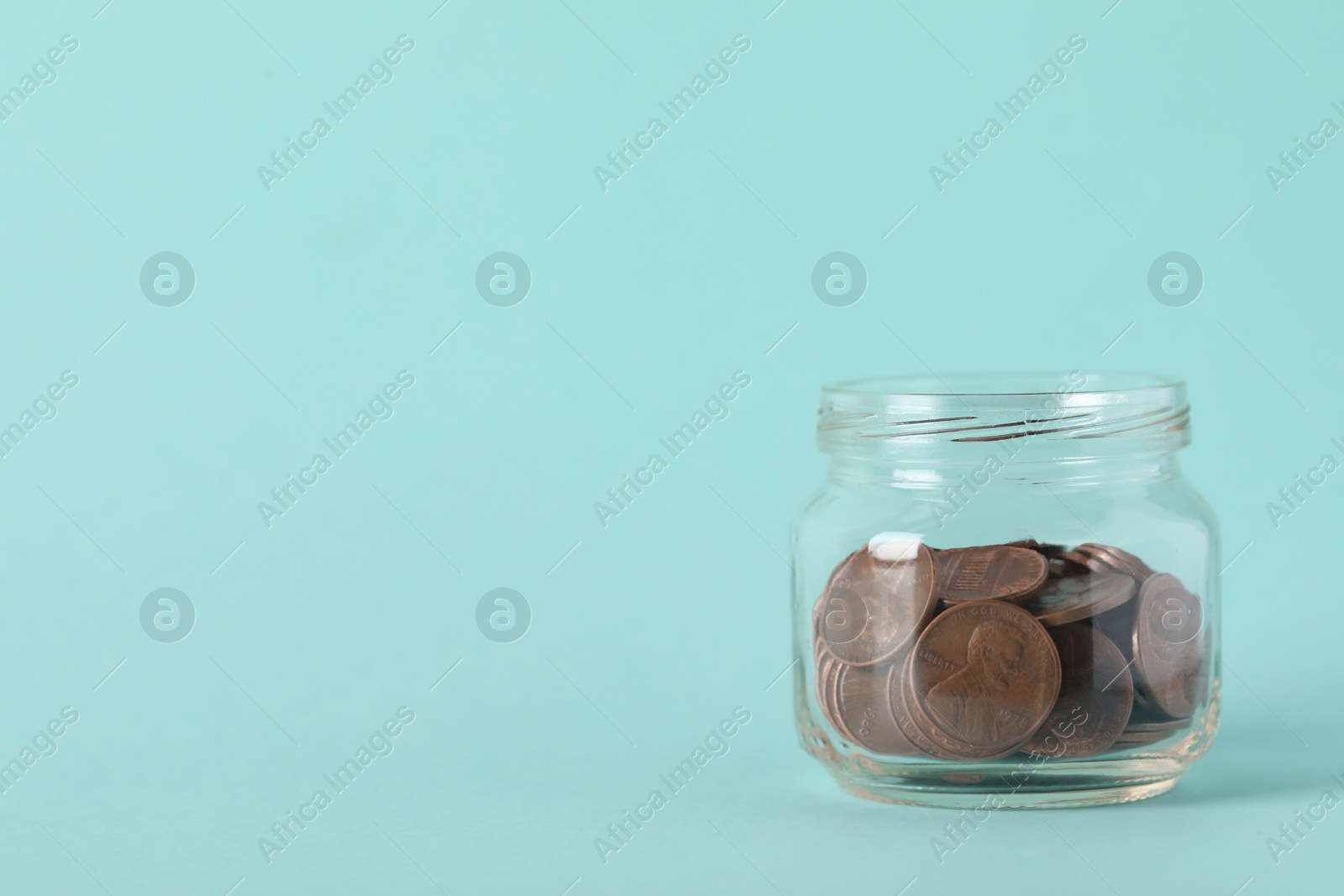 Photo of Glass jar with coins on light blue background, closeup. Space for text