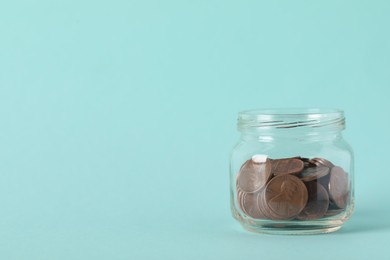 Glass jar with coins on light blue background, closeup. Space for text