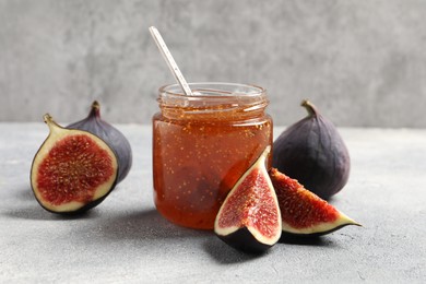 Glass jar with tasty sweet jam and fresh figs on light grey table