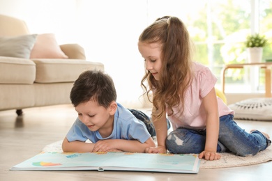 Photo of Cute children reading book on carpet in living room