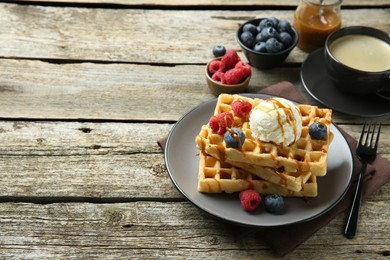 Photo of Delicious Belgian waffles with ice cream, berries and caramel sauce on wooden table, space for text