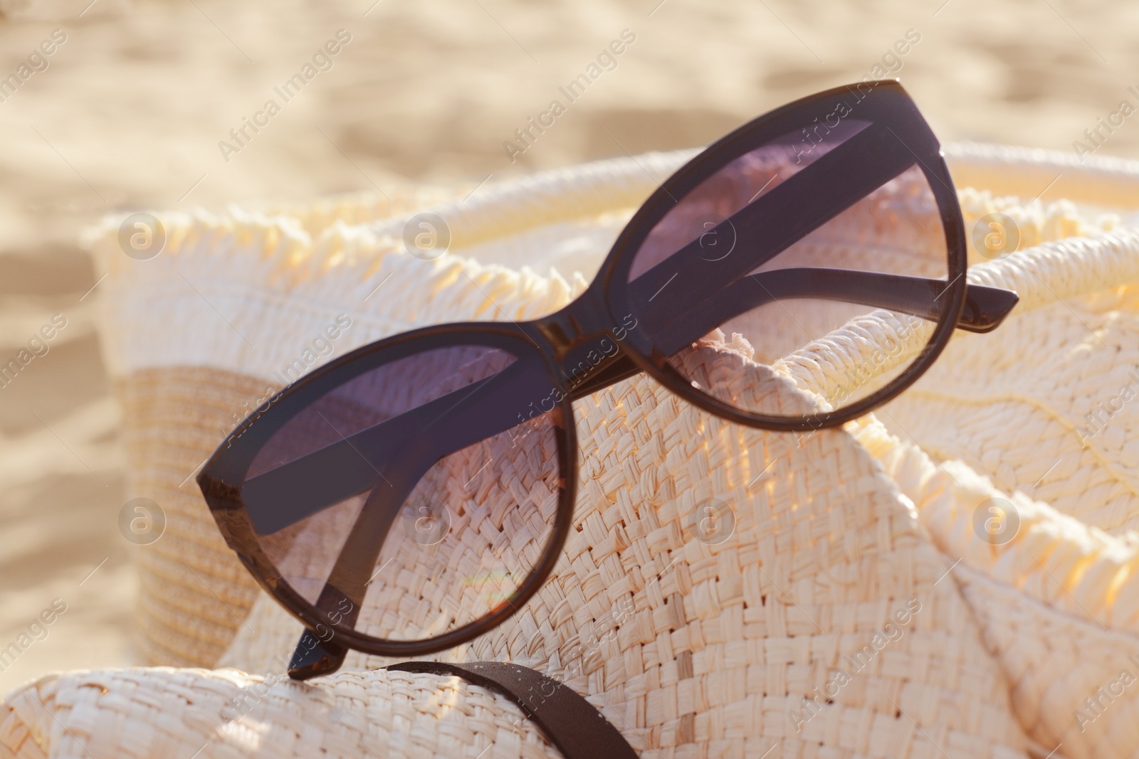 Photo of Hat and bag with beautiful sunglasses on sandy beach, closeup