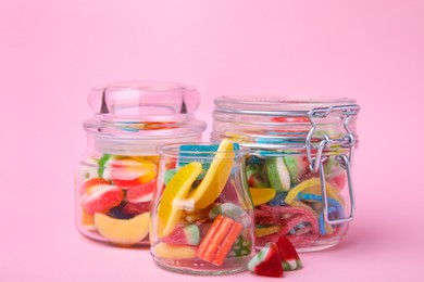 Photo of Tasty jelly candies in jars on pink background, closeup