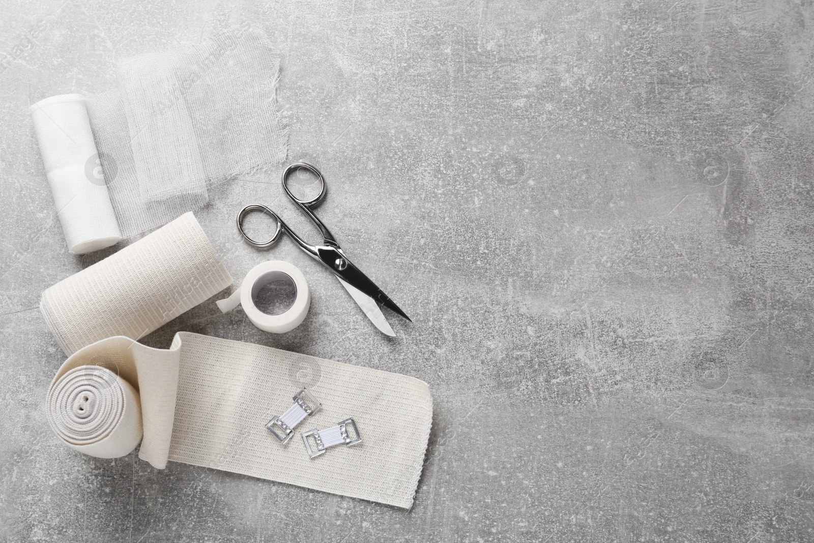 Photo of Medical bandage rolls, sticking plaster and scissors on grey table, flat lay. Space for text