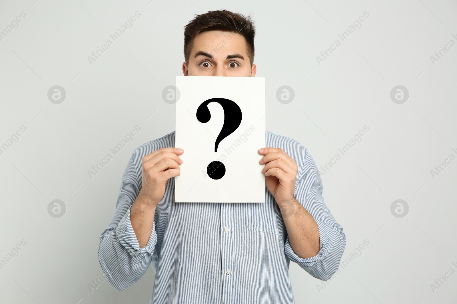 Photo of Emotional man holding question mark sign on light background