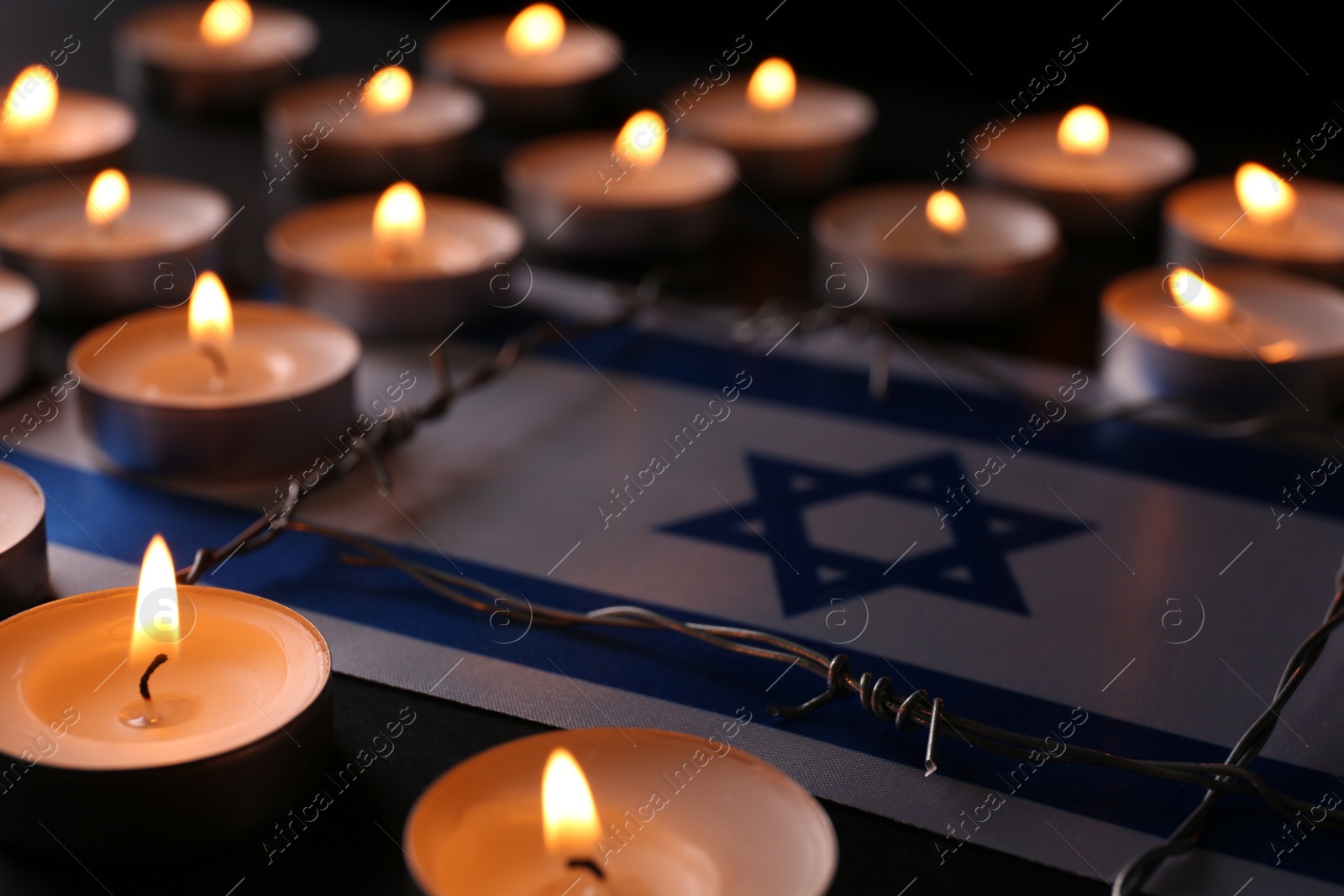 Photo of Flag of Israel, barbed wire and burning candles on black background. Holocaust memory day