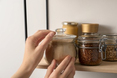 Photo of Woman taking glass jar of buckwheat flour from shelf, closeup
