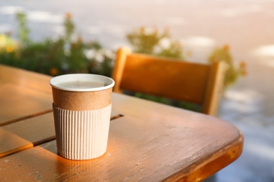 Cardboard coffee cup on wooden table outdoors. Space for text