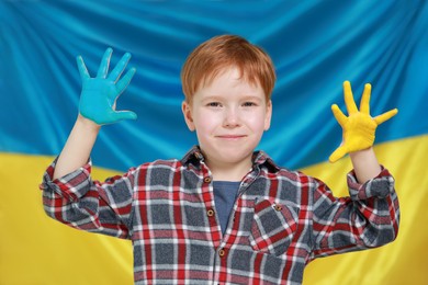 Photo of Little boy with painted hands near Ukrainian flag. Love Ukraine concept