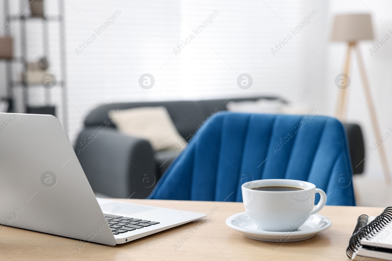 Photo of Home workspace. Laptop, cup of coffee and stationery on wooden desk indoors