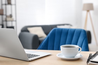 Photo of Home workspace. Laptop, cup of coffee and stationery on wooden desk indoors