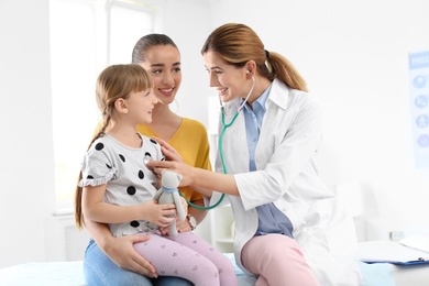 Photo of Children's doctor examining little girl near parent in hospital