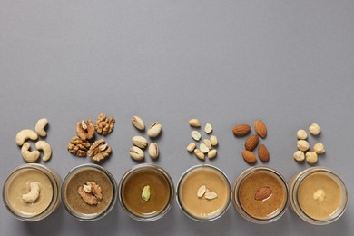 Photo of Tasty nut butters in jars and raw nuts on gray table, flat lay. Space for text