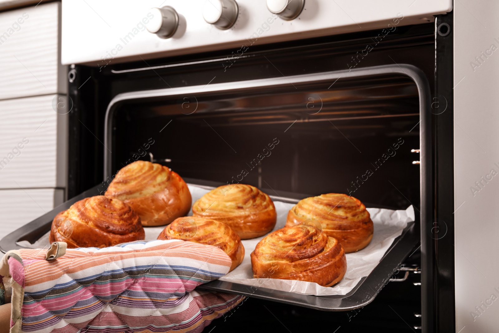 Photo of Woman taking freshly baked buns out of oven, closeup