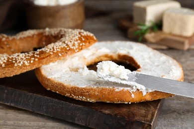 Photo of Delicious bagel with tofu cream cheese and knife on wooden table, closeup