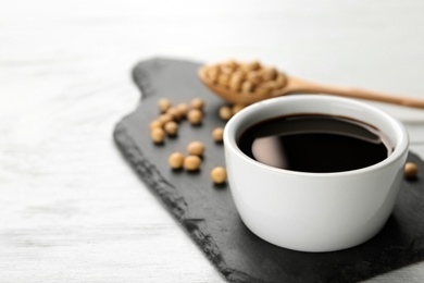 Slate board with bowl of soy sauce on wooden table. Space for text