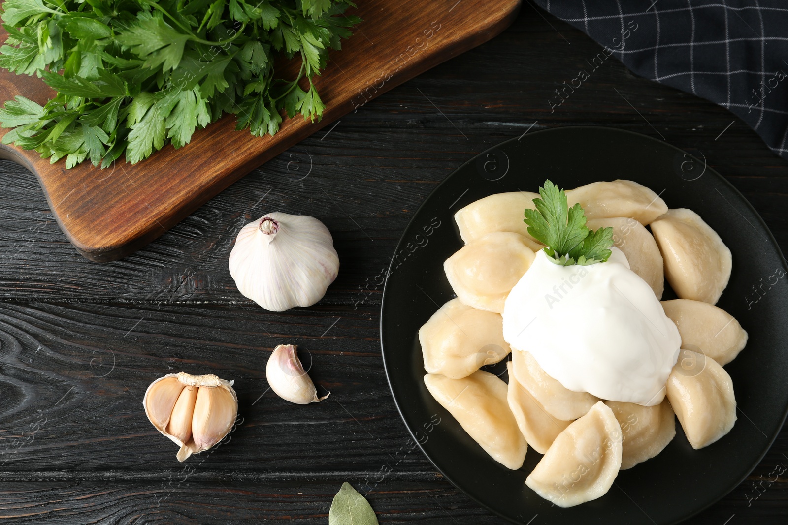 Photo of Delicious cooked dumplings with sour cream on dark wooden table, flat lay