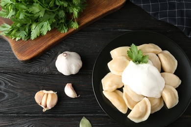 Photo of Delicious cooked dumplings with sour cream on dark wooden table, flat lay