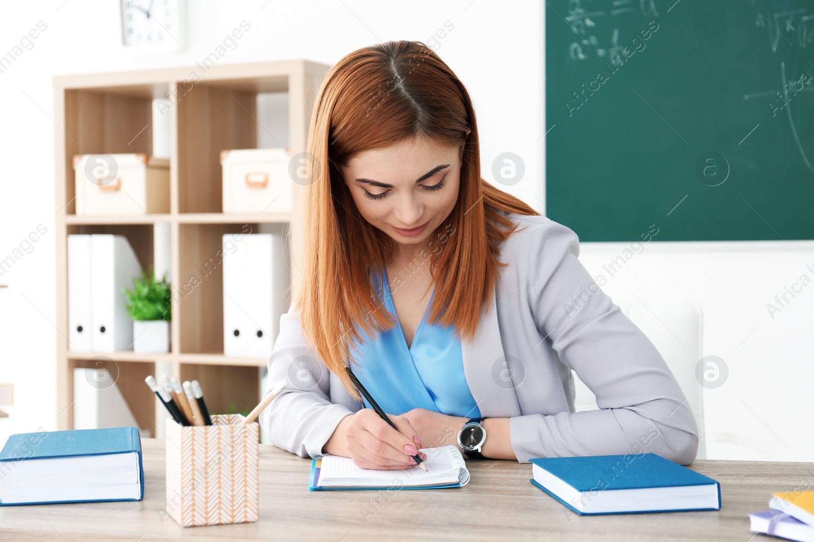 Photo of Beautiful young teacher working at table in classroom