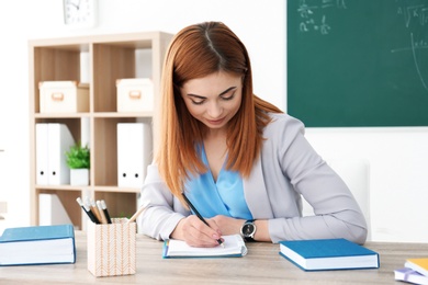 Photo of Beautiful young teacher working at table in classroom