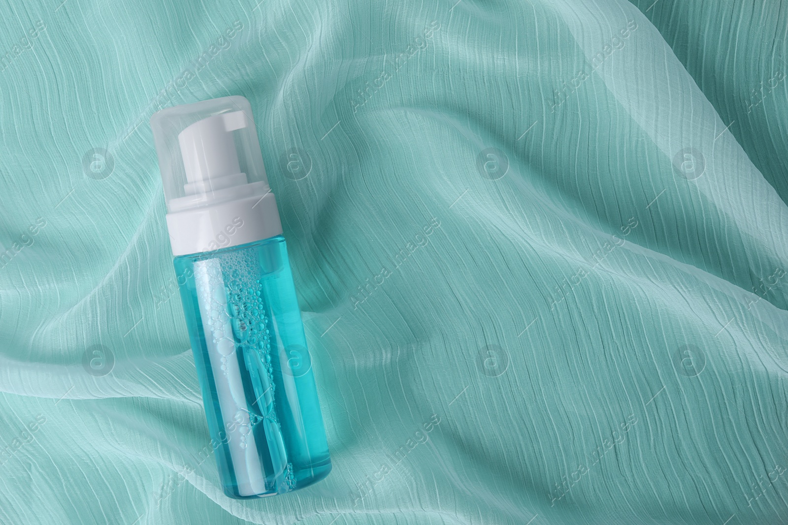 Photo of Bottle of face cleansing product on turquoise fabric, top view. Space for text