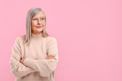 Photo of Portrait of beautiful middle aged woman in eyeglasses with crossed arms on pink background, space for text