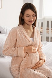 Happy young pregnant woman in bathrobe on bed at home