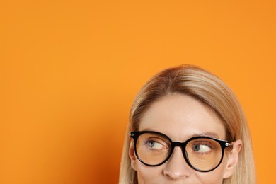 Photo of Woman in glasses looking out against orange background, closeup. Space for text