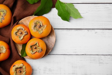 Photo of Delicious ripe juicy persimmons on white wooden table, flat lay. Space for text
