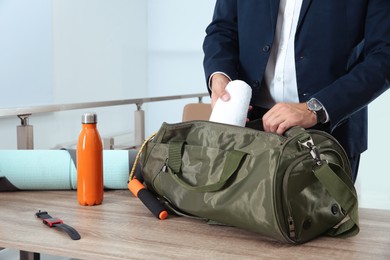 Photo of Businessman packing sports stuff for training into bag in office, closeup