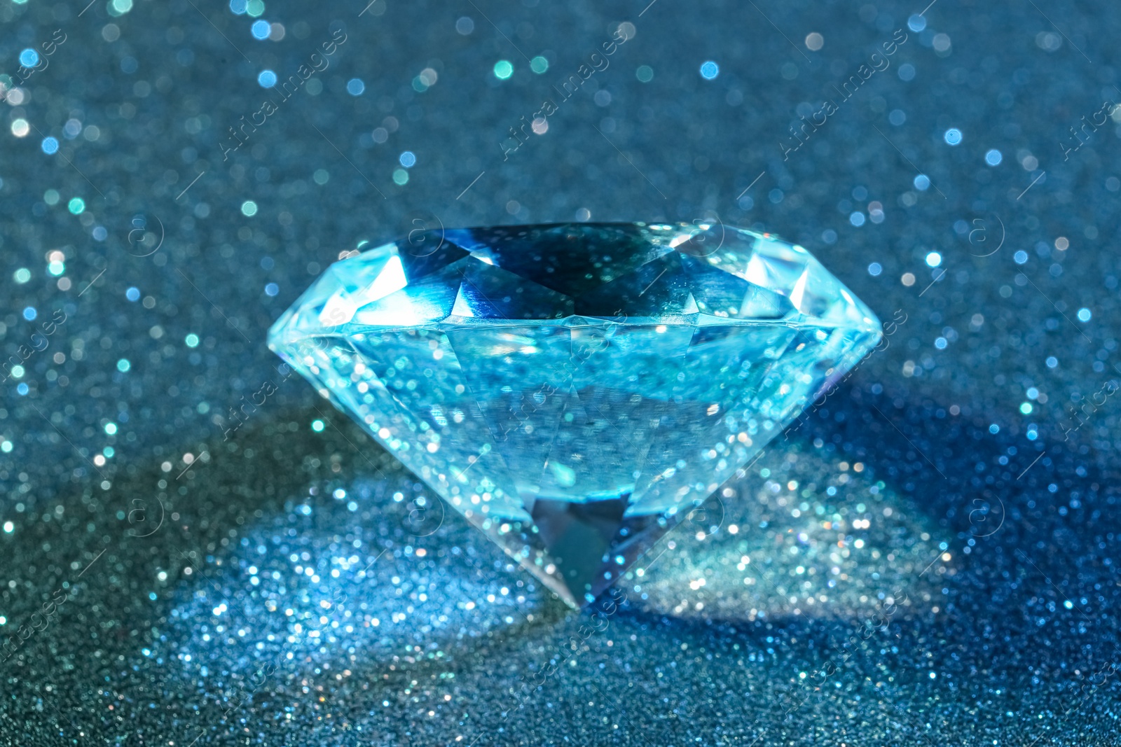 Photo of Beautiful dazzling diamond on light blue glitter background, closeup