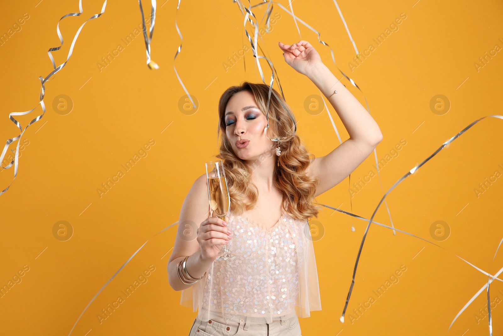 Photo of Happy woman with champagne and falling down serpentines on yellow background