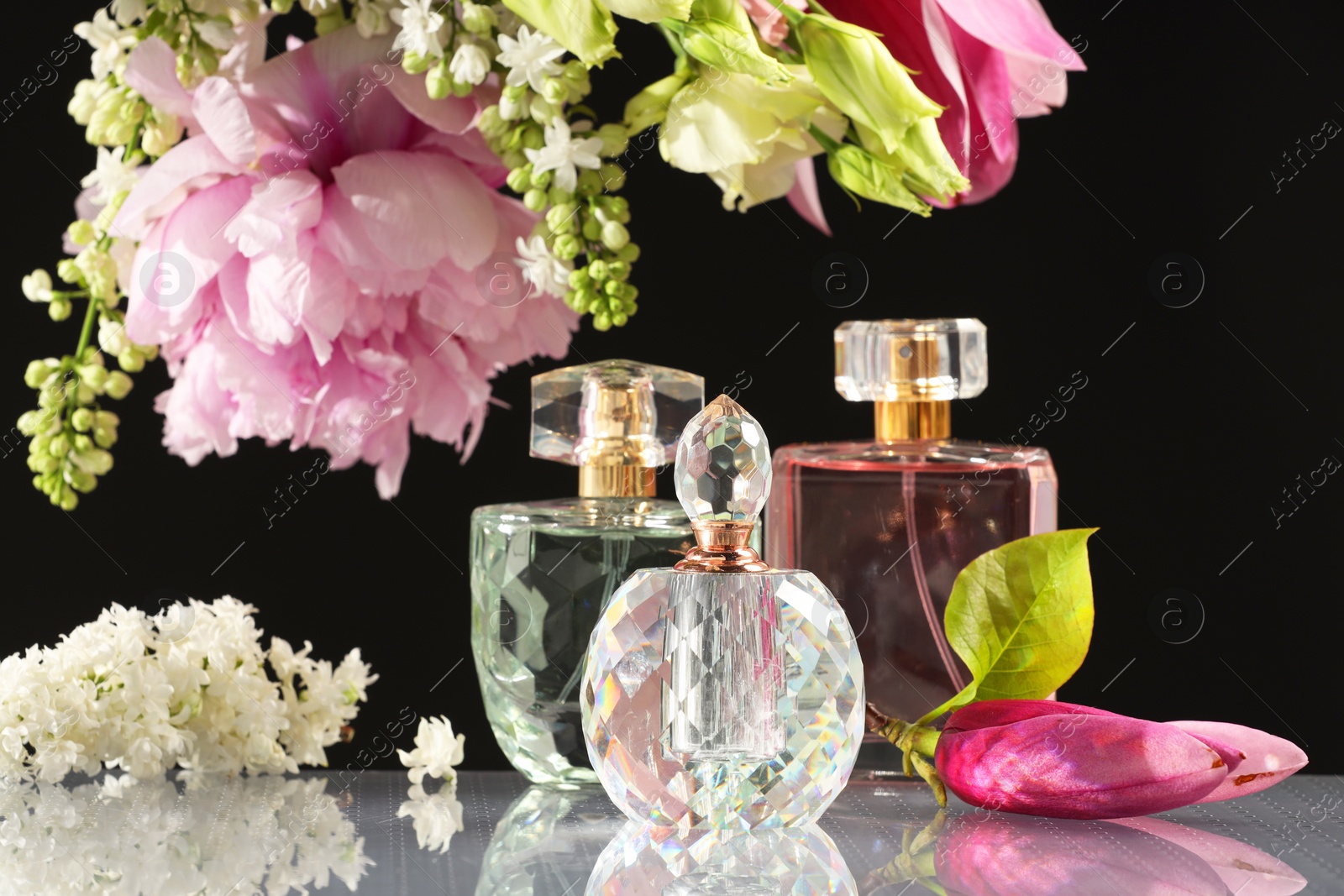 Photo of Luxury perfumes and floral decor on mirror surface against black background