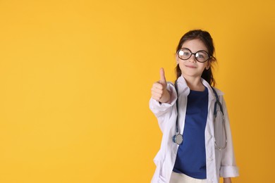 Photo of Little girl with eyeglasses and stethoscope dressed as doctor on yellow background, space for text. Pediatrician practice