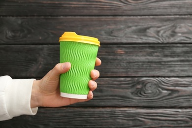 Woman holding takeaway paper coffee cup on wooden background. Space for text