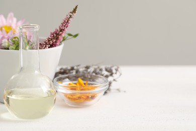 Photo of Developing cosmetic oil. Flask and flowers on white table, space for text