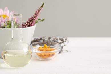 Developing cosmetic oil. Flask and flowers on white table, space for text