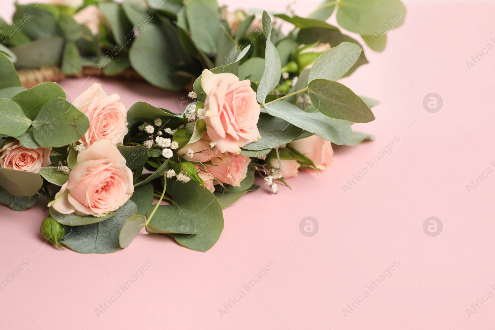 Photo of Wreath made of beautiful flowers on pink background, closeup. Space for text