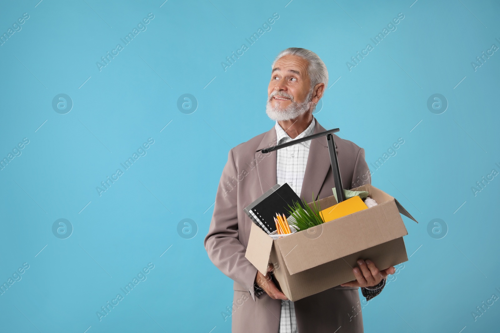 Photo of Happy unemployed senior man with box of personal office belongings on light blue background. Space for text