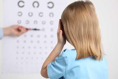 Ophthalmologist testing little girl's vision in clinic, back view