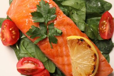 Photo of Tasty grilled salmon with tomatoes, lemon and basil on white background, top view