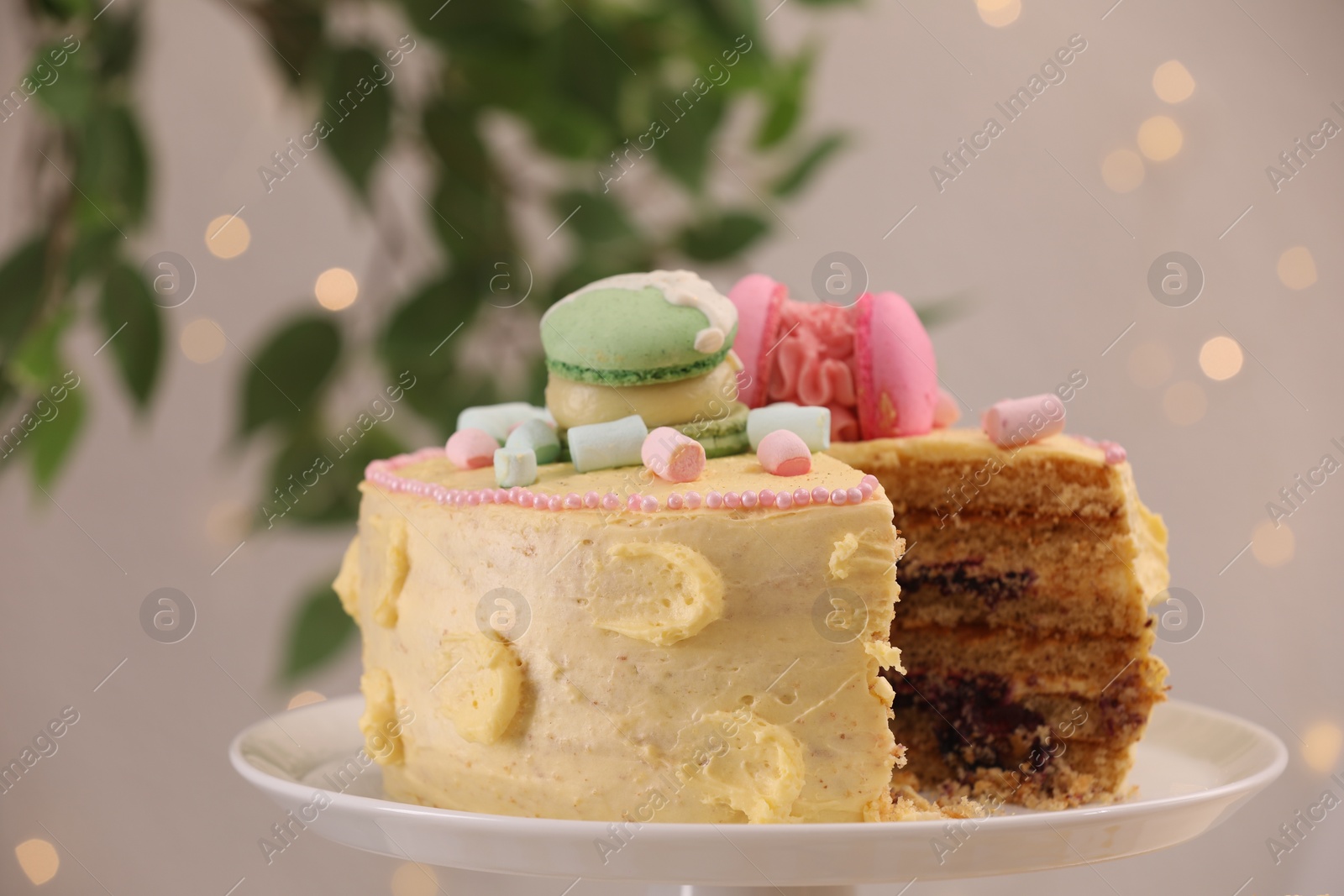 Photo of Delicious cake decorated with macarons and marshmallows against blurred lights, closeup