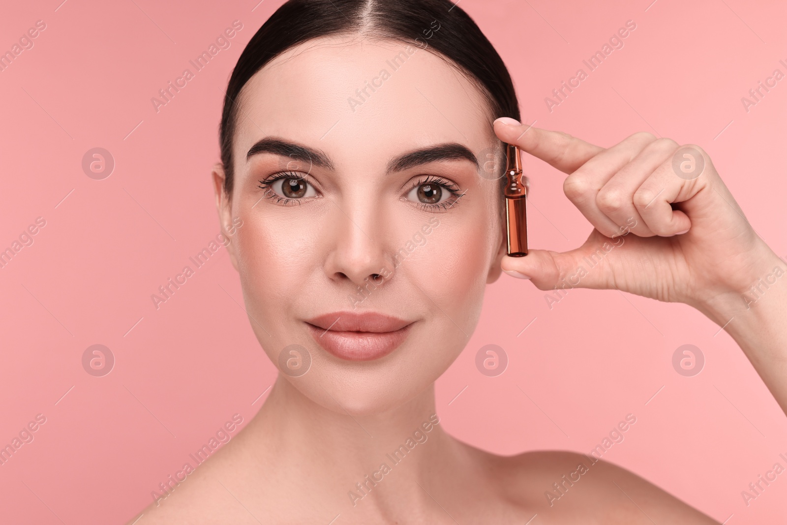 Photo of Beautiful young woman holding skincare ampoule on pink background