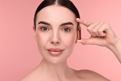 Beautiful young woman holding skincare ampoule on pink background