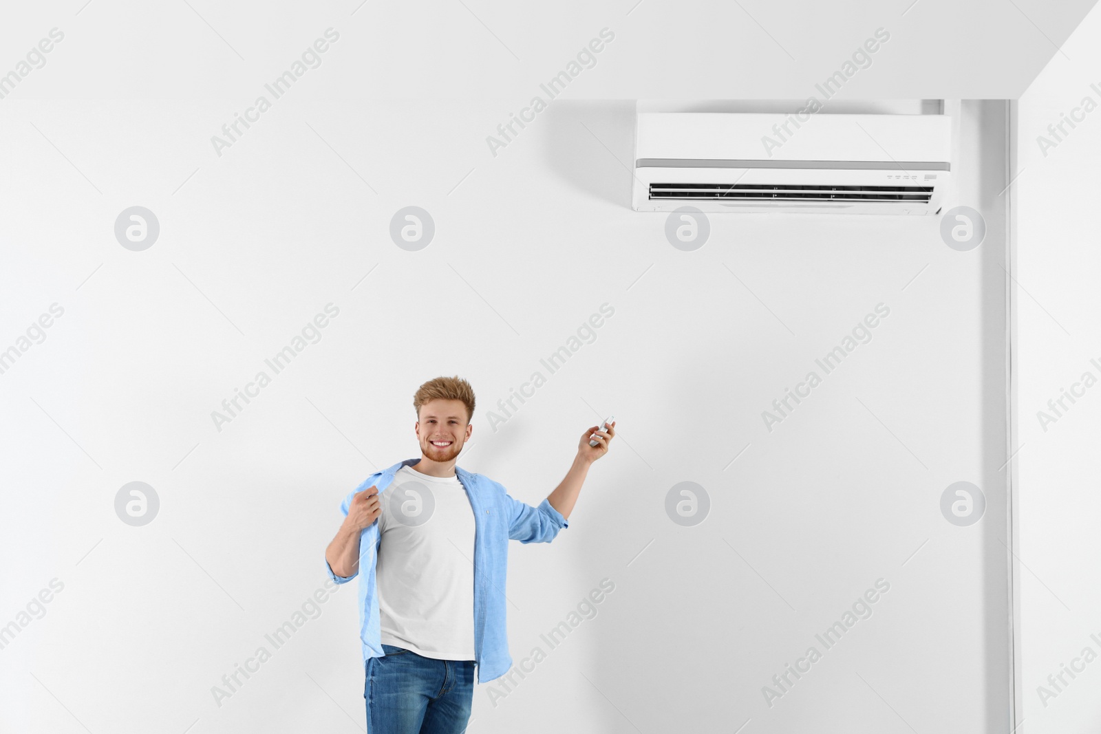 Photo of Young man operating air conditioner with remote control indoors. Space for text