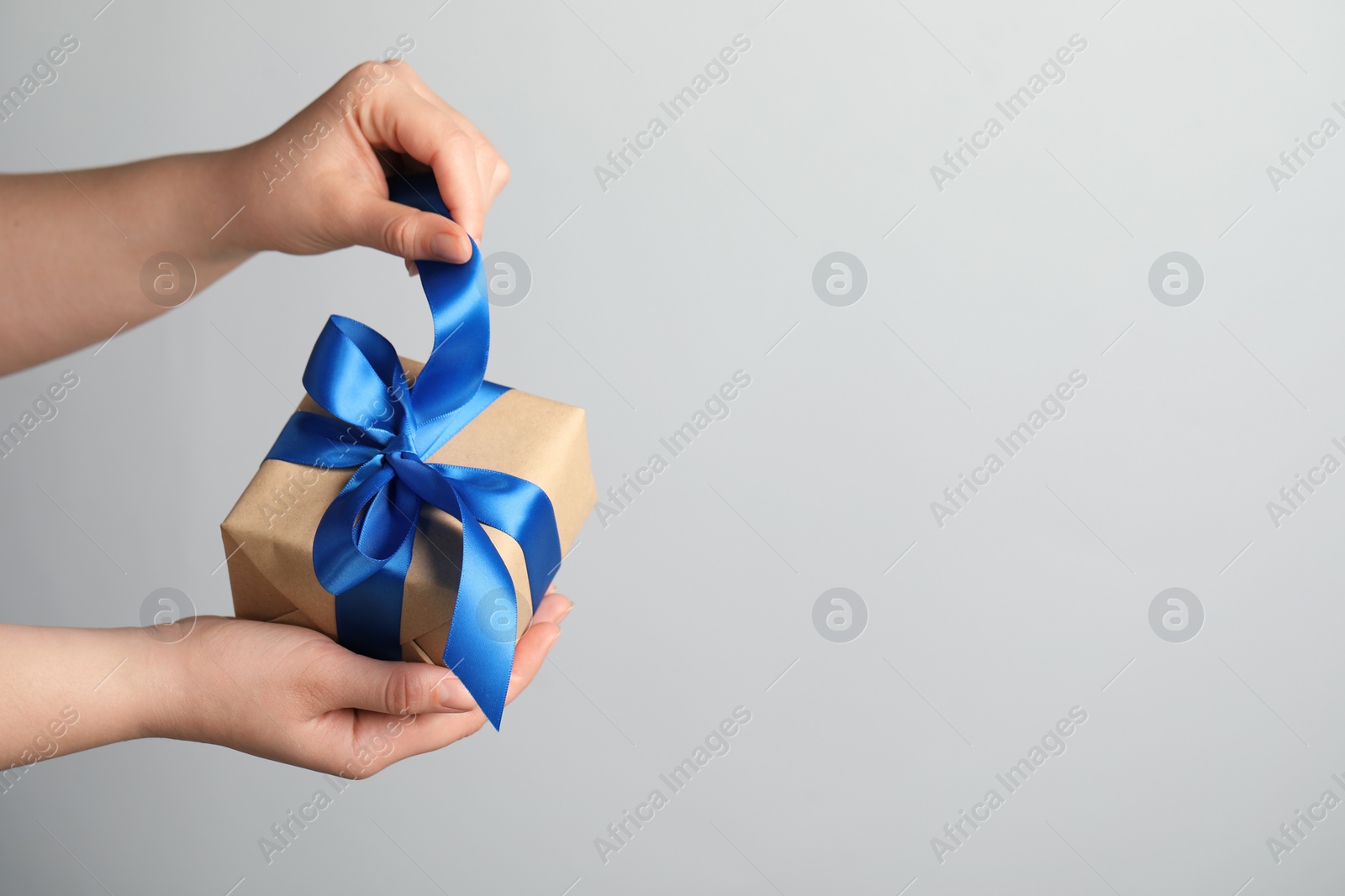 Photo of Woman holding gift box with blue bow on light grey background, closeup. Space for text