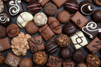 Photo of Different delicious chocolate candies on black table, flat lay