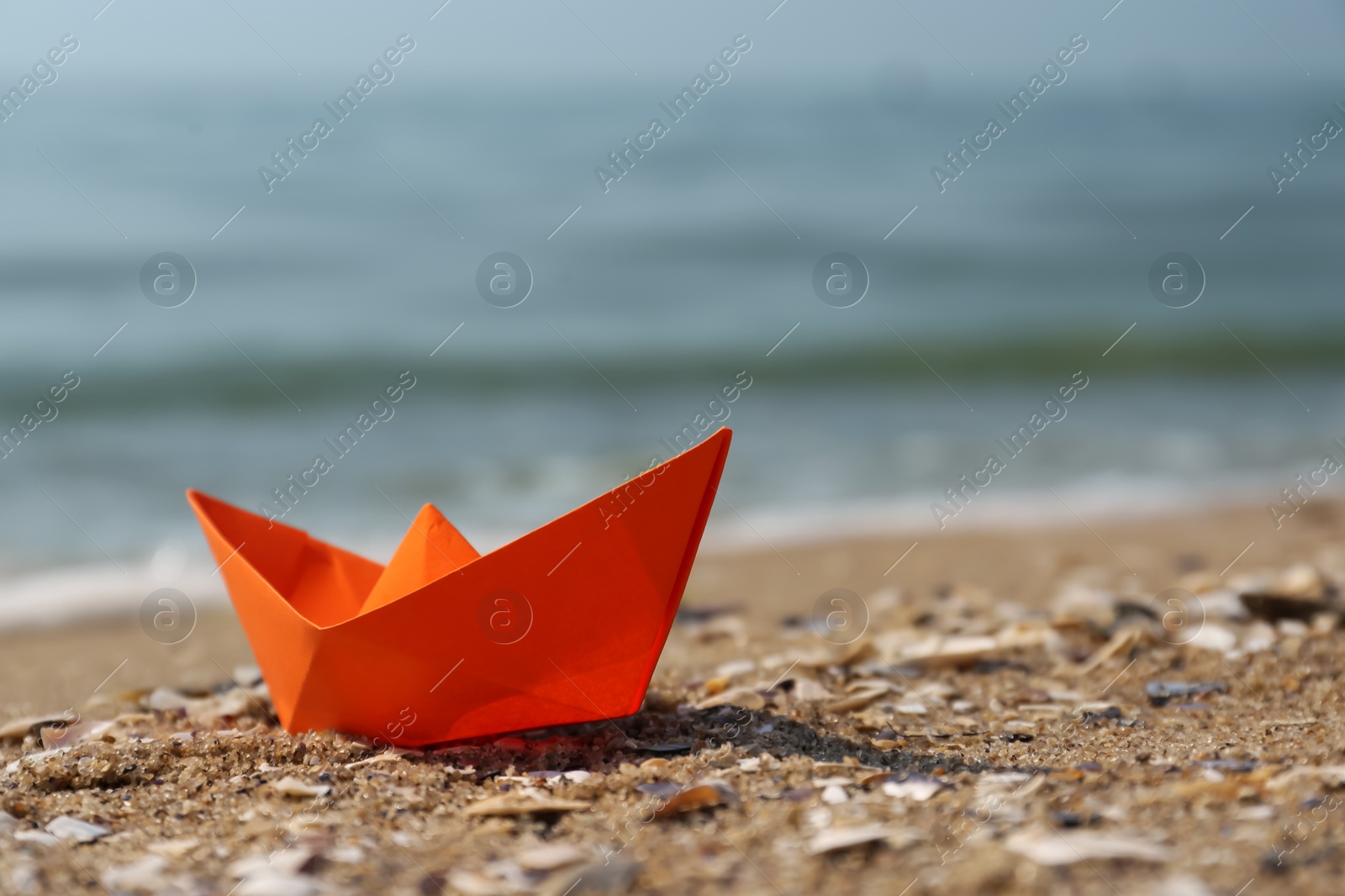 Photo of Orange paper boat on sandy beach near sea, space for text