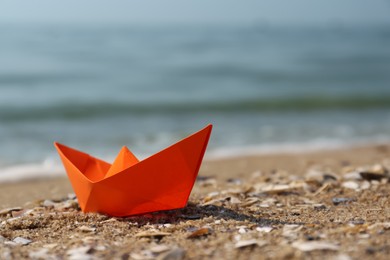 Photo of Orange paper boat on sandy beach near sea, space for text