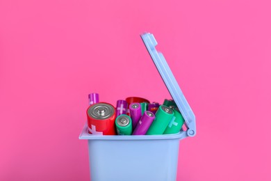 Many used batteries in recycling bin on pink background